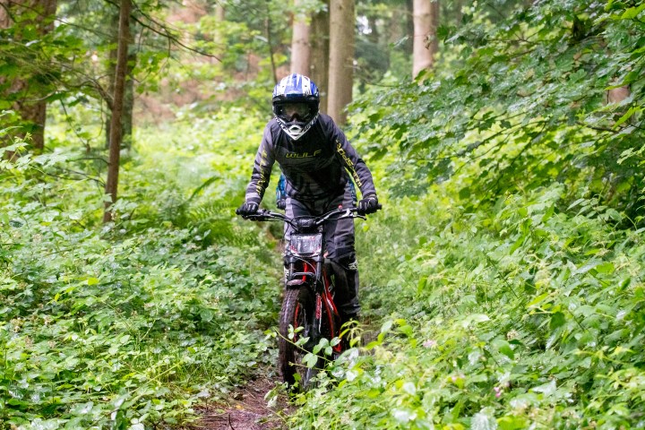 Biker in helmet riding through a forest trail surrounded by lush greenery.